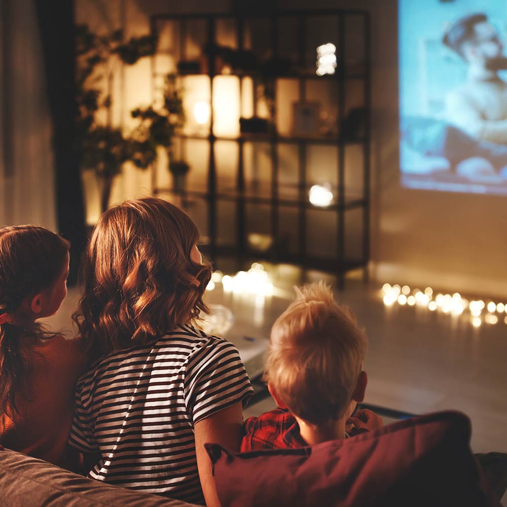 Familie sitzt auf Couch und schaut Film, Abendstimmung